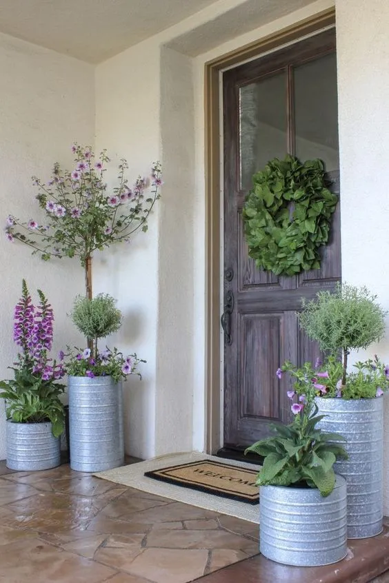 Galvanized metal planters filled with blooming flowers bring a farmhouse feel to your doorstep. Complement the look with a grapevine wreath on the door and textured foliage for a cohesive spring theme. This style feels both fresh and timeless.