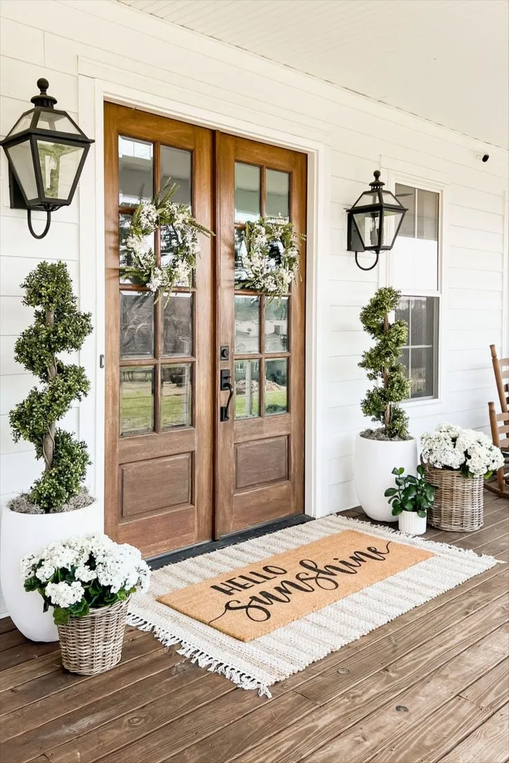 Enhance your home’s curb appeal with symmetrical wreaths and potted topiaries framing double doors. The “Hello Sunshine” doormat adds a friendly touch, while the white blooms in woven baskets exude elegance. This setup offers a classic, polished look that’s perfect for making a lasting first impression this spring.