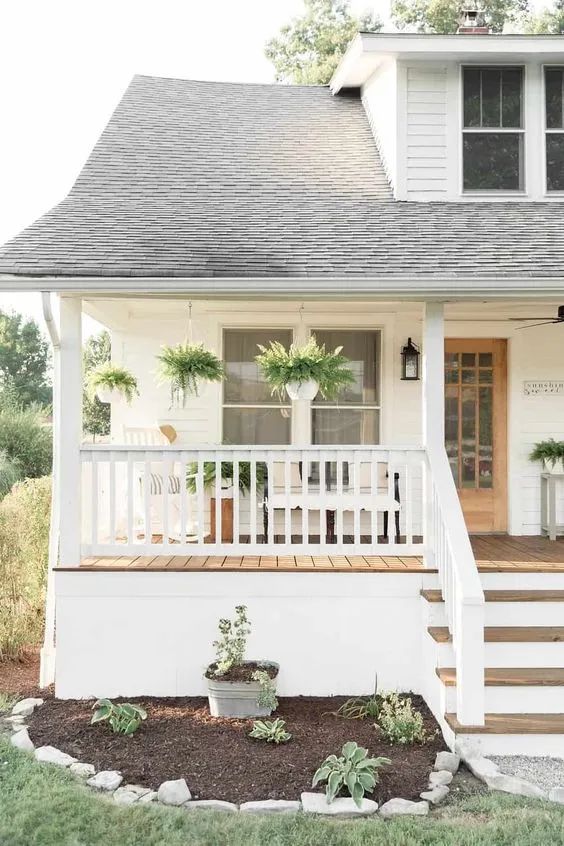 Simplicity shines with this minimalist porch setup featuring hanging ferns and neatly arranged planters. The white railings and wooden steps provide a neutral backdrop, allowing the vibrant green foliage to stand out. This decor is easy to maintain and perfect for those who prefer a clean, uncluttered outdoor look.